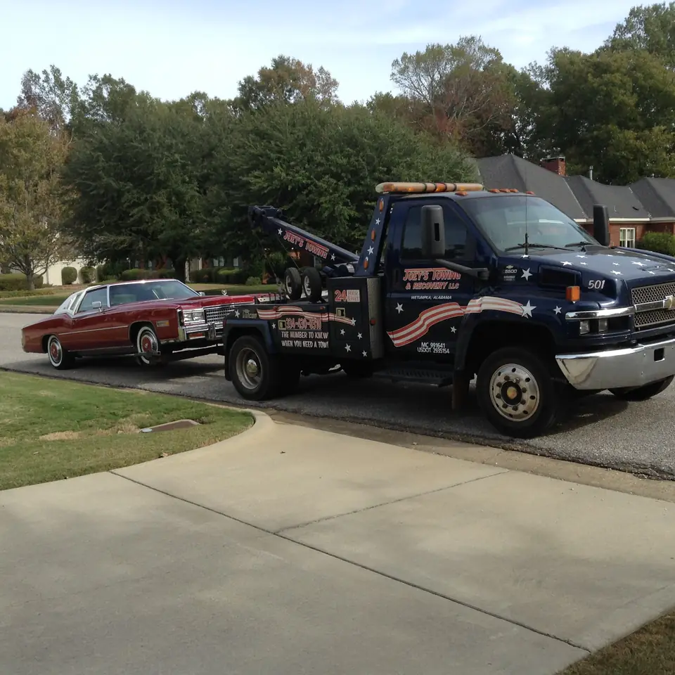 Joey's wrecker towing a red classic Cadillac through a neighborhood